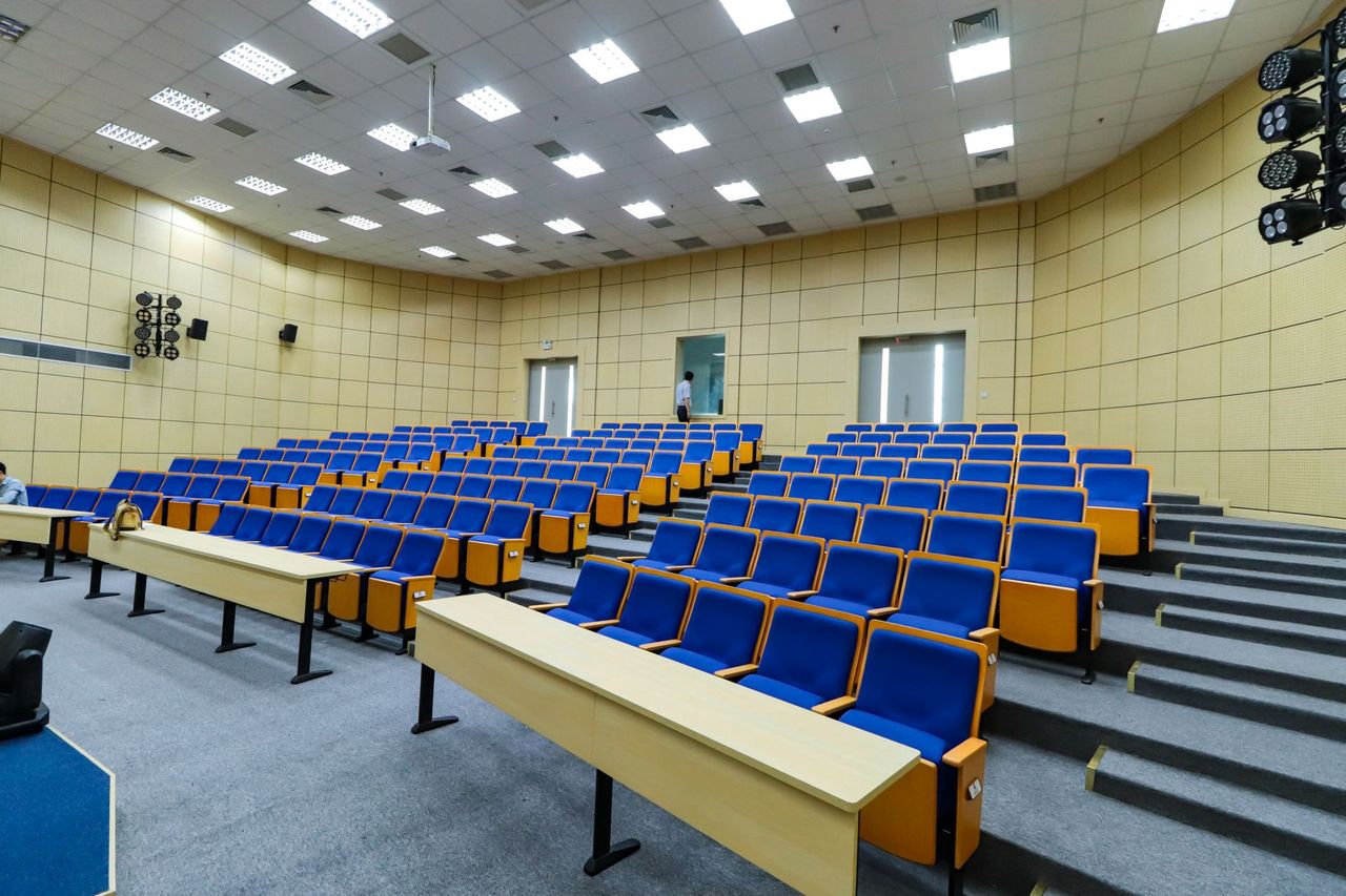 Lecture room with green chairs, writing desks and a projection area at the front.