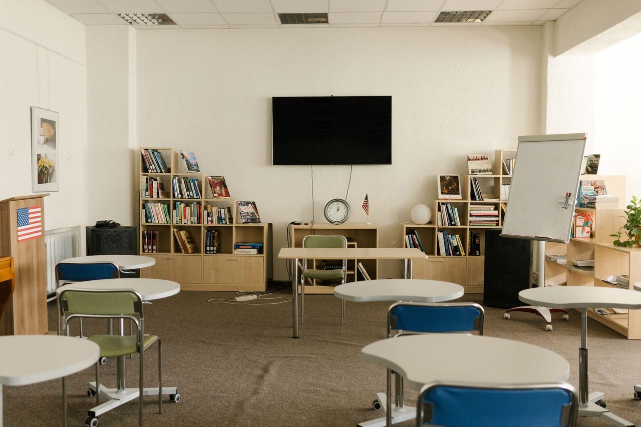 Bright classroom with individual desks, a whiteboard, a screen and bookshelves.